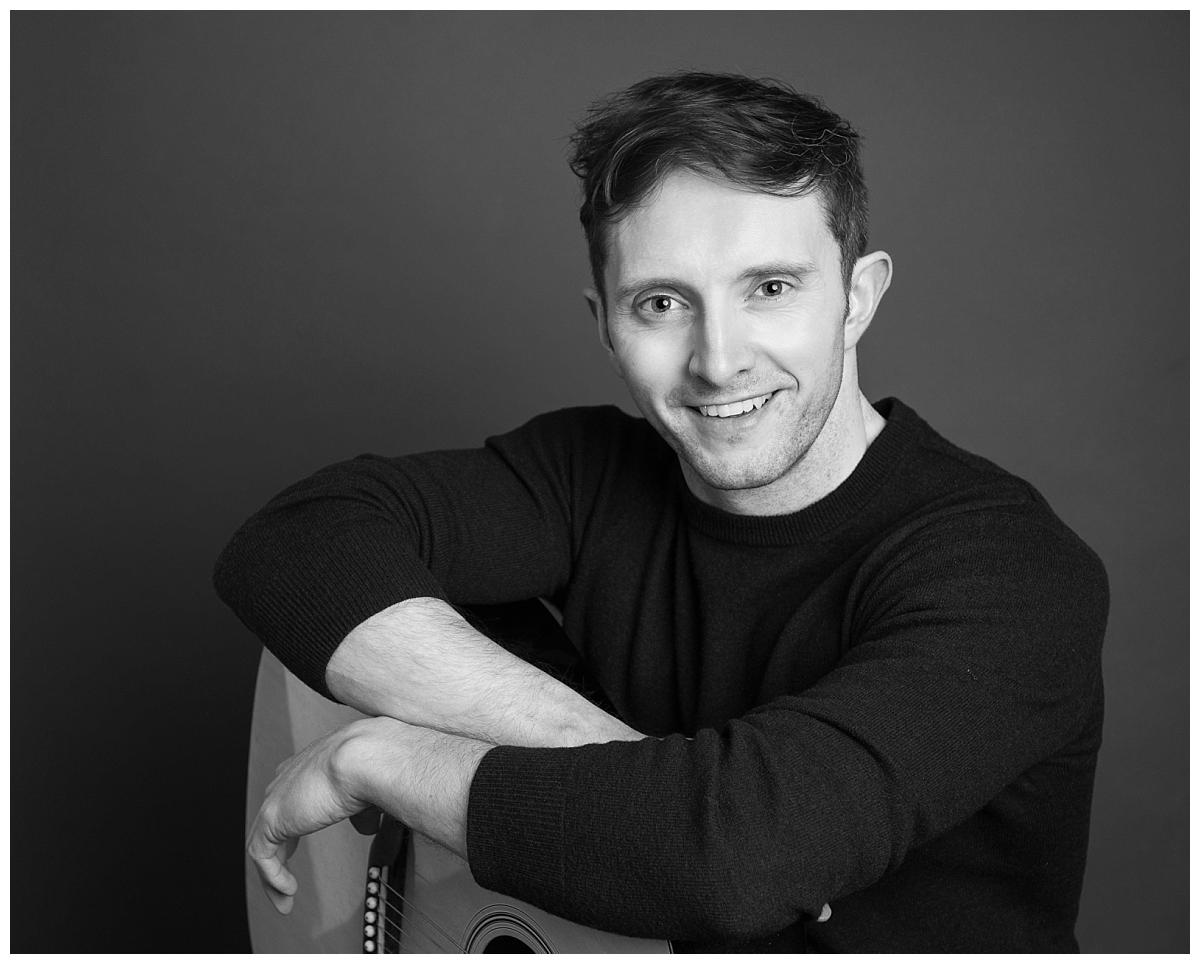 Professional headshot photograph taken by Northern Ireland's top headshot photographer in Belfast of a guy with a guitar straight on to camera in Black an white