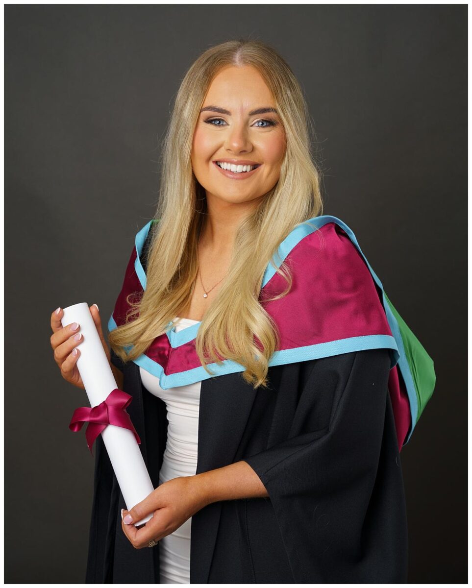 Professional Graduation photograph taken by Northern Ireland's top Graduation photographer in Belfast of a a girl in her Masters gowns from Queens University Belfast on a grey background
