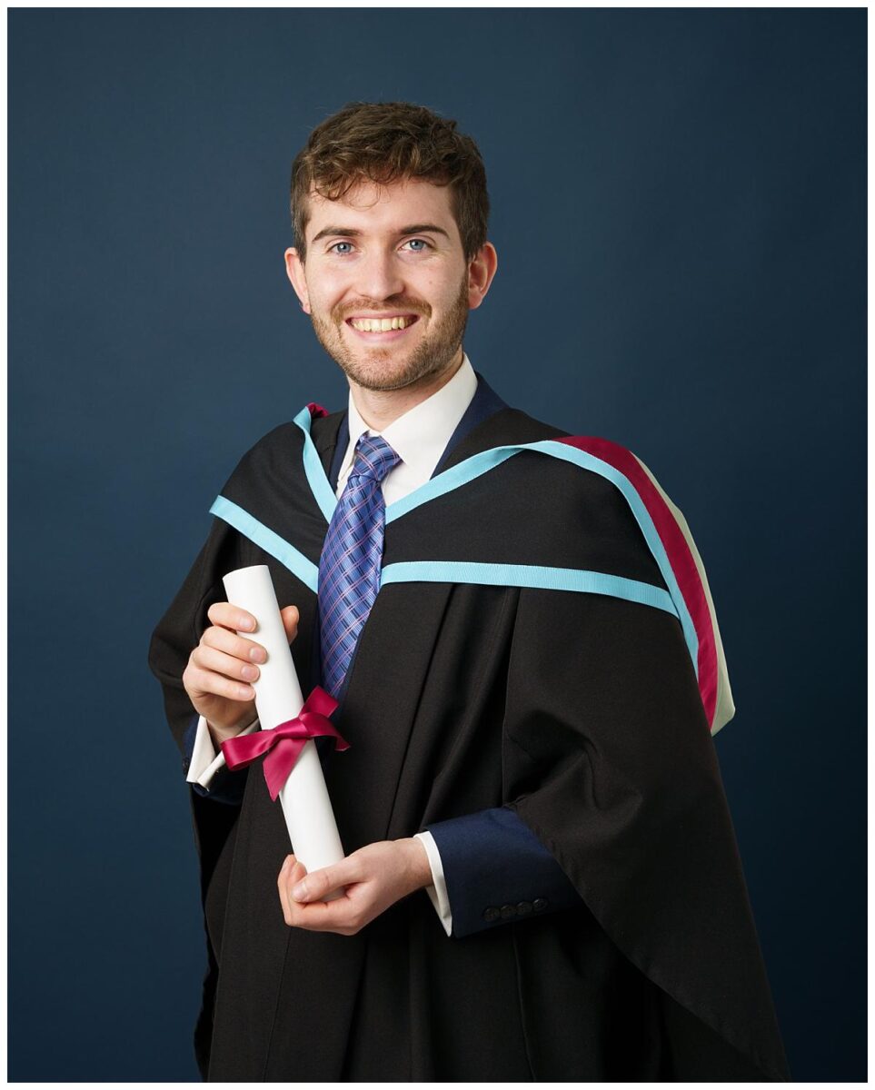 Professional Graduation photograph taken by Northern Ireland's top Graduation photographer in Belfast of a a Man wearing his masters gowns from Queens University on a navy blue background