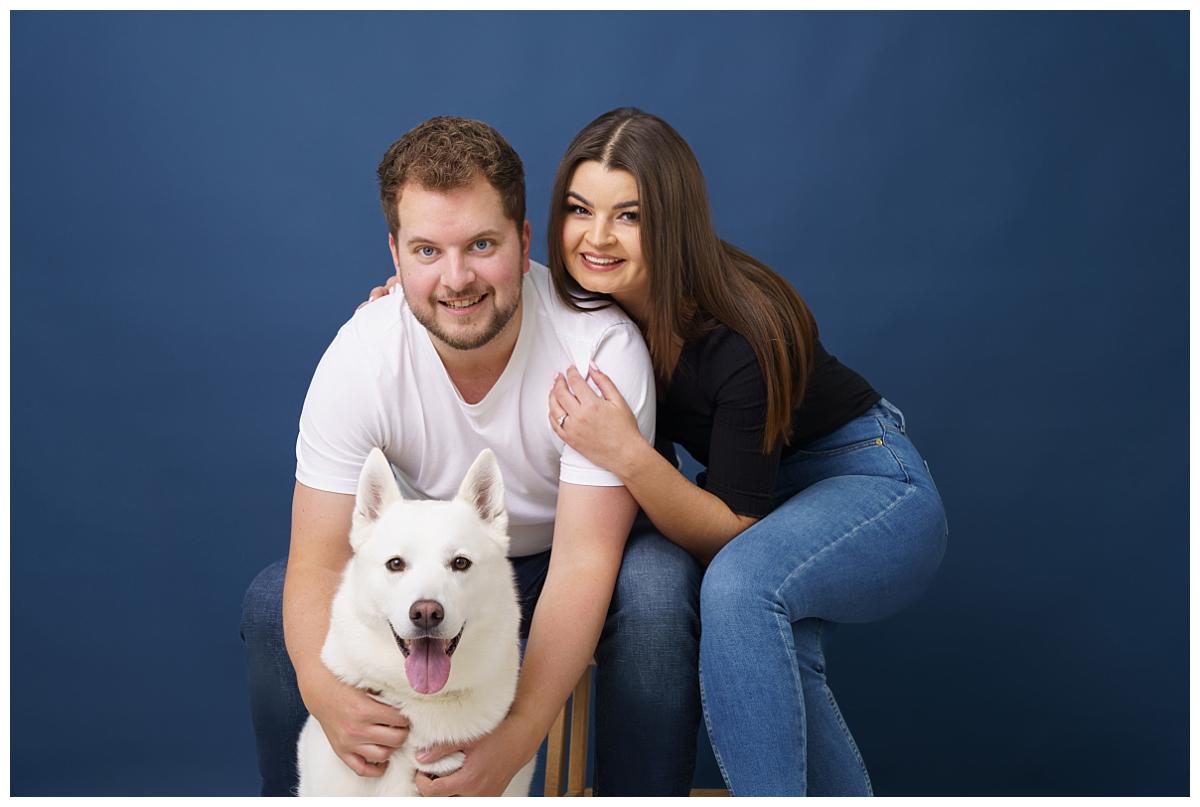 Professional pet photograph, taken by Northern Ireland's top pet photographer in Belfast of white German Shepherd with his 2 owners on a navy backdrop